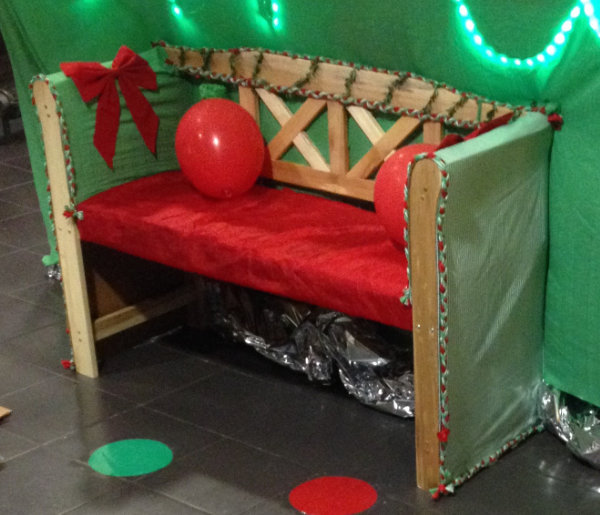 A picture of a wooden garden bench decorated with red and green fabric for a Chrismassy look. A pressure sensor on the seat triggers audio of Santa snoring.